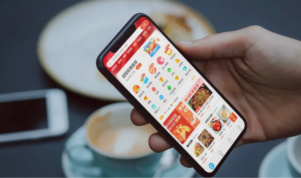Close-up of a smartphone showing the Pinduoduo shopping app interface with product listings and category icons