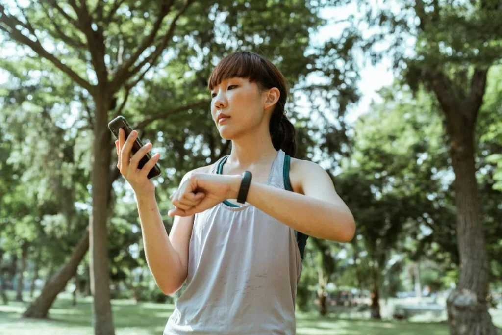Woman checking her smartphone and fitness tracker outdoors