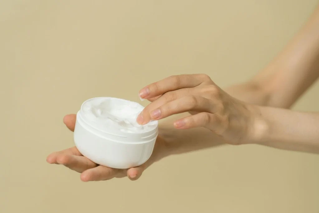 Hands holding an open skincare cream jar against a neutral background