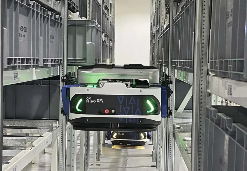 An automated warehouse robot moving through storage racks in a Chinese logistics facility.