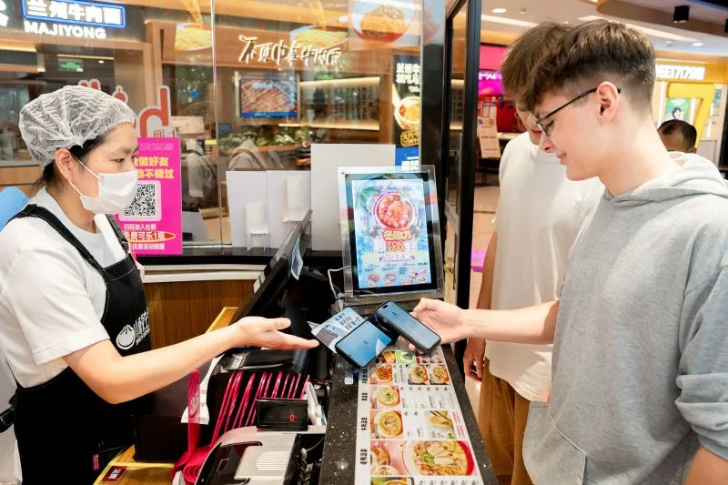 wechat pay for foreigners: Tourist paying with a phone at a restaurant checkout in China.