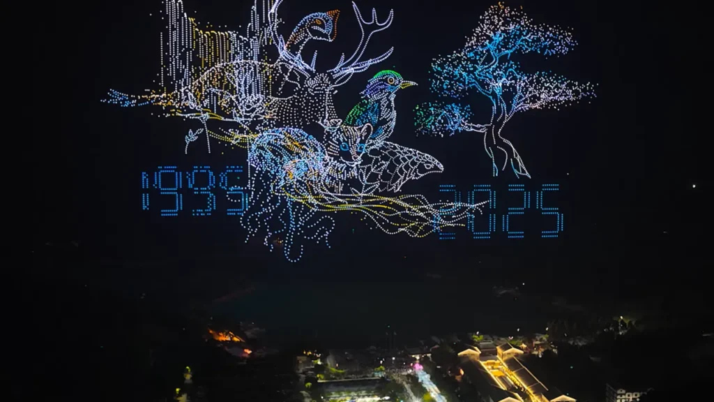Drone light show forming animals, trees, and the years 1935 and 2025.