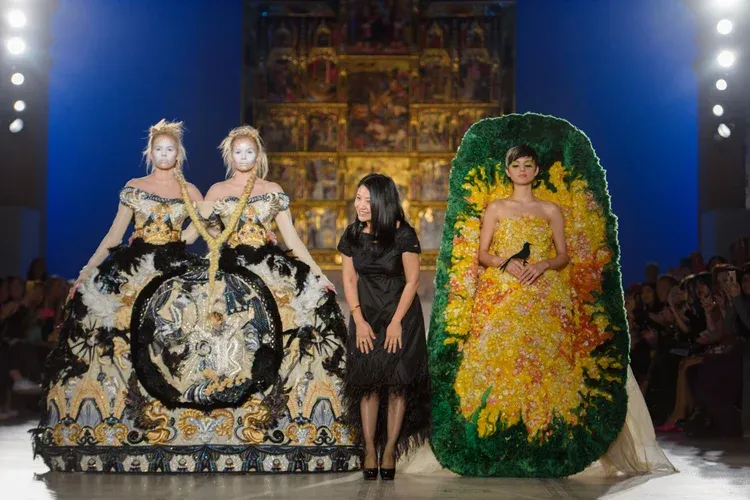 Designer standing with models in dramatic couture gowns