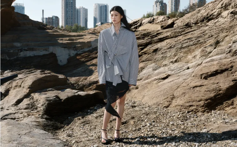 Model wearing layered JNBY outfit on rocky ground