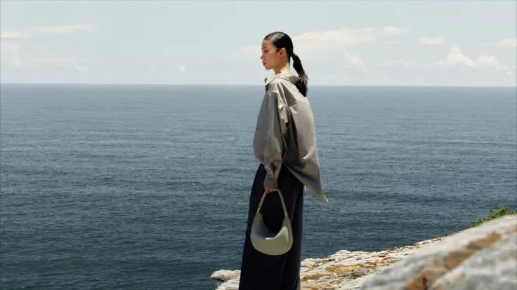 Model holding a crescent bag by the sea