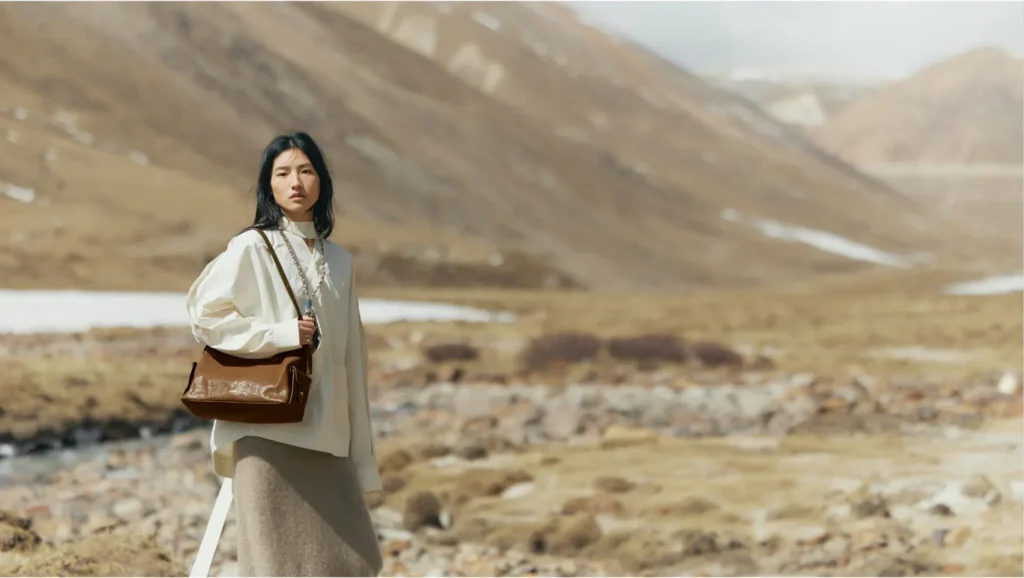Model carrying a brown shoulder bag in the mountains