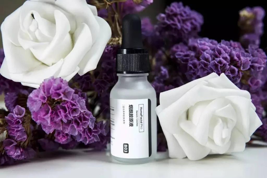 HomeFacialPro serum bottle placed between white roses and purple flowers