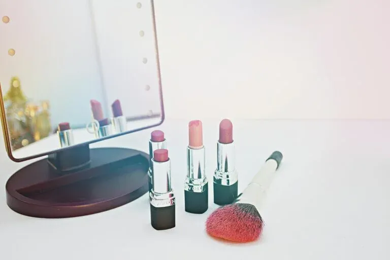 Lipsticks and makeup brush placed beside a mirror
